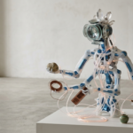 Uma escultura robótica humanoide translúcida de design minimalista, composta por engrenagens visíveis e cabos de fibra ótica, manuseando delicadamente objetos orgânicos e tecnológicos sobre um pedestal branco em um ambiente de arquitetura escandinava com luz natural suave.